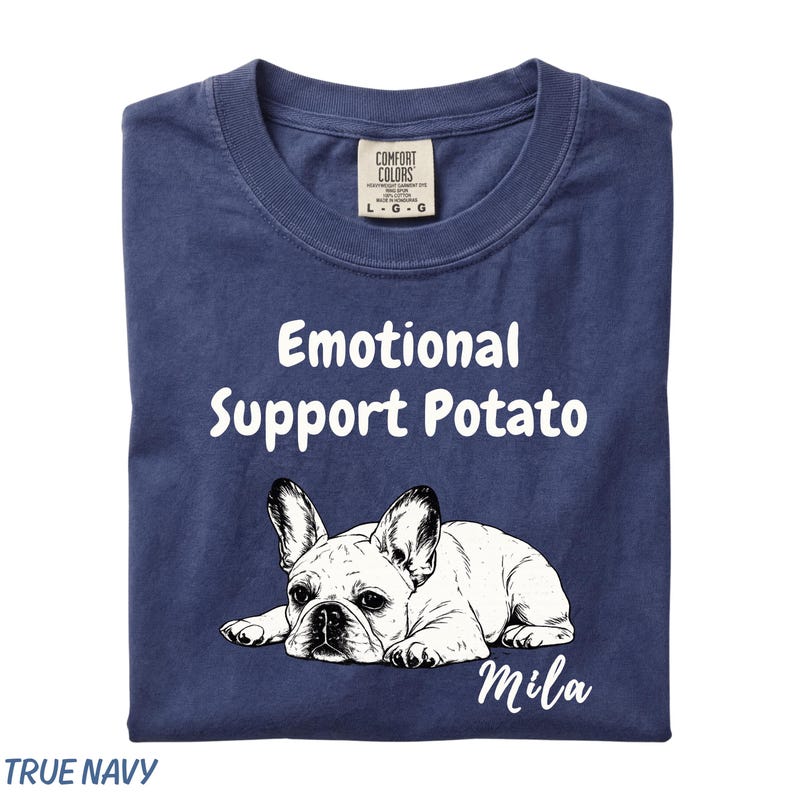 May include: A navy blue t-shirt featuring the white text "Emotional Support Potato" above a black and white line drawing of a French Bulldog lying down, with the name "Mila" written in white script below the dog and a Comfort Colors brand label.