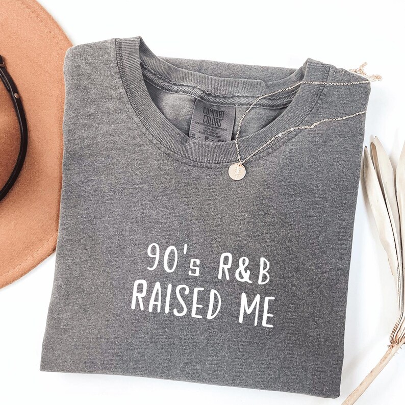 Puede incluir: Camiseta gris con el texto "90's R&B RAISED ME" en blanco.
