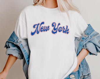 May include: White t-shirt with a blue and red "New York" graphic in a retro font.