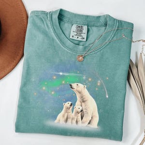 May include: A teal blue t-shirt with a graphic of three polar bears looking up at the aurora borealis. The shirt has a tag that reads "Comfort Colors" and "Heather Garment Dye".