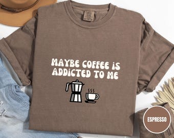 May include: Espresso-colored t-shirt with the text "MAYBE COFFEE IS ADDICTED TO ME" in white, along with a black and white illustration of a coffee pot and a cup of coffee. The shirt is a Comfort Colors brand.