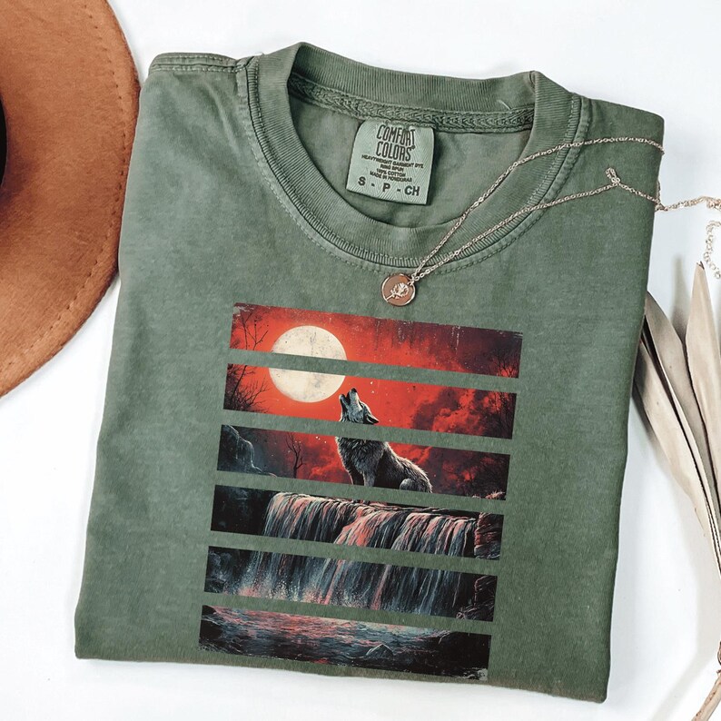 May include: A green t-shirt with a wolf howling at the moon graphic. The graphic is layered with red, orange, and black stripes. The t-shirt has a tag that says "Comfort Colors" and "S - P - CH".