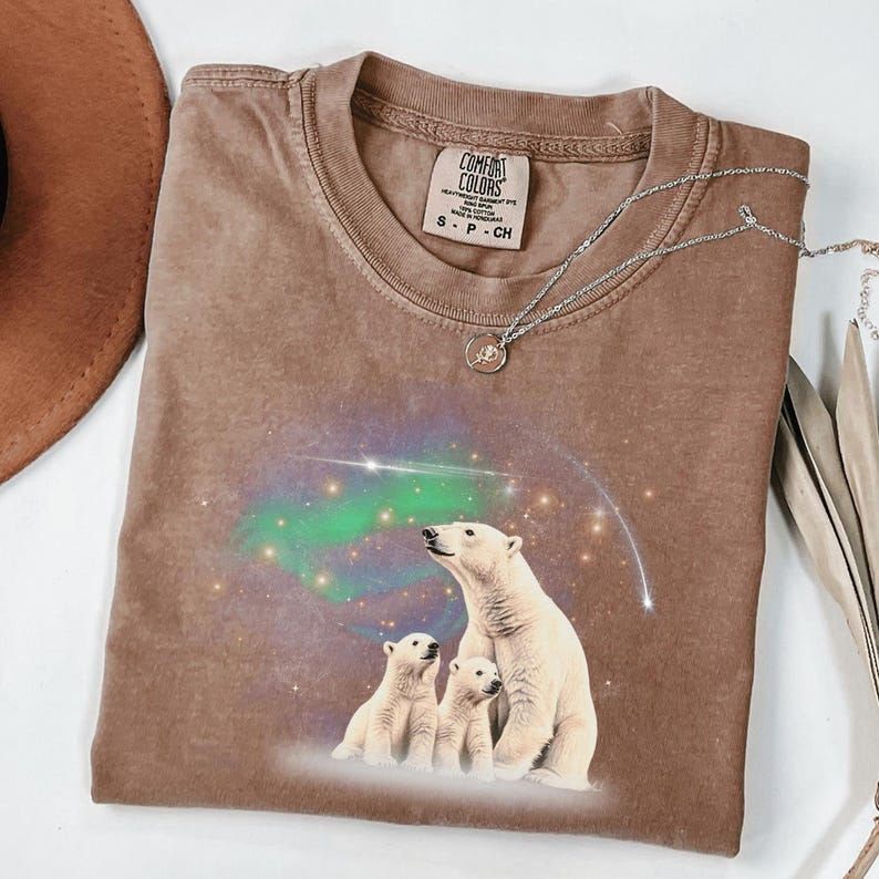 May include: A brown t-shirt with a graphic of three polar bears looking up at a green and purple aurora borealis. The shirt has the text "COMFORT COLORS" and "S - P - CH" on the tag.