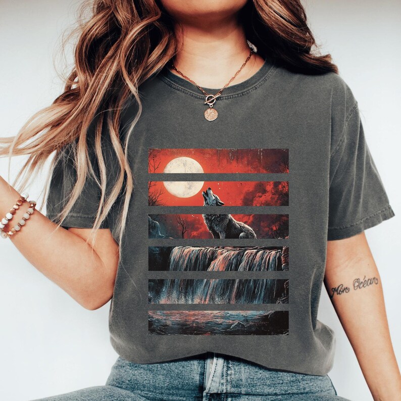 May include: A gray t-shirt with a graphic print of a wolf howling at the moon. The graphic is divided into horizontal stripes with a red sky, a waterfall, and a body of water. The text "More Oceans" is visible on the right sleeve.