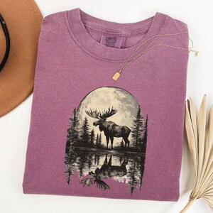 May include: Purple t-shirt with a graphic of a moose standing in a lake with a full moon behind it. The text "COMFORT COLORS" is on the tag.