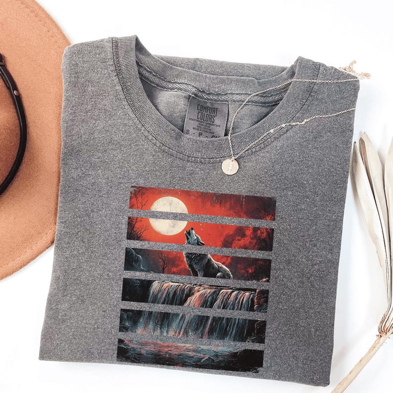 May include: Gray t-shirt with a graphic print of a wolf howling at the moon in front of a waterfall. The graphic is divided into horizontal stripes with a red sky and a full moon.