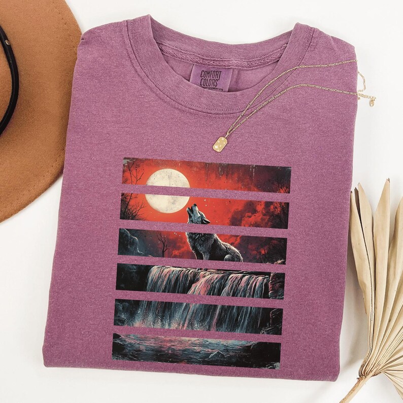May include: A purple t-shirt with a graphic of a wolf howling at the moon with a waterfall in the background. The graphic is made up of horizontal stripes.
