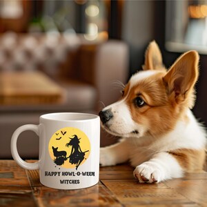 May include: White ceramic coffee mug with a black silhouette of a witch and a dog flying on a broomstick in front of a yellow moon. The text "Happy Howl-O-Ween Witches" is printed on the mug.
