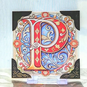 May include: A square decorative piece with the letter "P" in a stained-glass design. The letter is red with gold detailing, set against a blue and white background with floral and scroll patterns. Black corner protectors are attached.