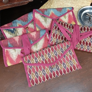 May include: Five small, colorful fabric pouches with pink trim and decorative buttons. The pouches have a variety of geometric patterns in shades of red, blue, gold, and white.
