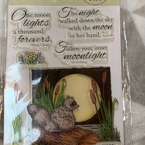 May include: Clear stamp set featuring a raccoon sitting on a log with a full moon in the background. Includes quotes: "One moon lights a thousand forevers" and "The night walked down the sky with the moon in her hand."