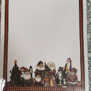 May include: A rectangular sheet of stationery paper featuring a white center framed by a dark green and red border. The bottom section displays a group of illustrated figures resembling Santa Claus in various outfits, a Christmas tree, and a small penguin.