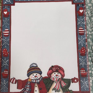 May include: A rectangular sheet of stationery featuring a white center bordered by a blue frame with white snowflakes and red mittens. At the bottom, two illustrated snowmen stand side-by-side, wearing winter hats, scarves, and coats.