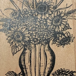 May include: A black and white line drawing of a vase filled with sunflowers and other flowers. The vase has a striped pattern and is sitting on a table with a leaf on the side.