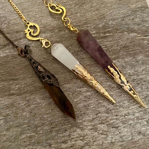 Pendoli divinatori molto belli, uno in ametista dorata con punta grande. Un pendolo in oro e selenite, un pendolo in rame con occhio di tigre. Regali