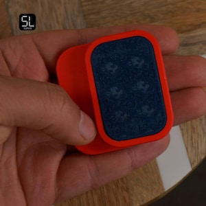 May include: A red and blue rectangular object with rounded corners. The object has a dark blue surface with a pattern of small, light-coloured shapes. The object is held in a person's hand.