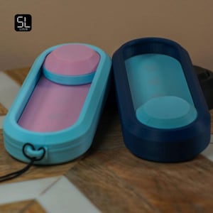 May include: Two oval-shaped, 3D-printed containers. One is light blue with a pink interior and a pink circular top. The other is dark blue with a light blue interior and a light blue circular top. Both have a small hole and a black string.