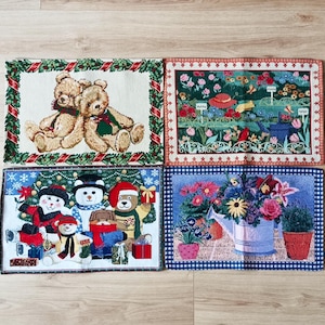 Könnte beinhalten: Vier dekorative rechteckige Matten mit verschiedenen Designs. Eine zeigt zwei Teddybären mit Schals, eine andere eine Gartenszene, eine Weihnachtsszene mit Bären und eine Gießkanne mit Blumen.
