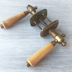 May include: Two vintage door handles. They feature brass fittings and light-coloured wooden handles. The handles are rectangular with a rounded end. The brass plates are rectangular with screw holes. Likely for a cabinet or door.