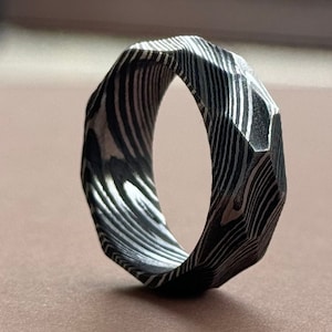 May include: A silver ring with a geometric, faceted design. The ring is made of a patterned metal with a black and white striped pattern.