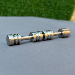 May include: A silver-colored metal fidget toy with a cylindrical design. The toy features a series of stacked rings and rounded end caps connected by a central rod. The surface has a polished, reflective finish, and the toy is set against a gray background.