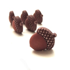 May include: A group of six brown acorn-shaped buttons with a textured top. The buttons are arranged in a line, with the largest button at the front.