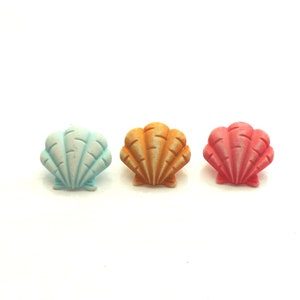 May include: Three seashell buttons in different colors: light blue, orange, and pink. The buttons are arranged in a row from left to right.
