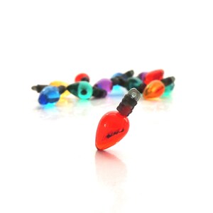 May include: A group of colorful miniature Christmas lights, with one red light in the foreground. The lights are scattered on a white surface.