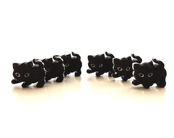 May include: Six black plastic cat figurines in a row, each with white eyes and a slightly different pose.