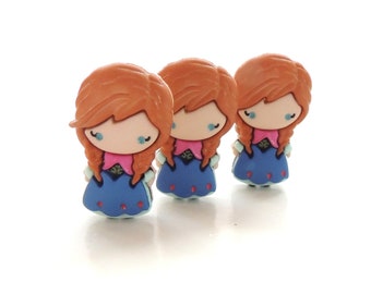 May include: Three small plastic figurines of a girl with red hair, wearing a blue dress with white accents. The figurines are arranged in a row, facing forward.