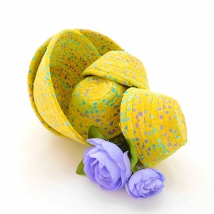 May include: A set of four yellow woven baskets with a blue and green speckled pattern. The baskets are nested inside each other and are decorated with two purple flowers.
