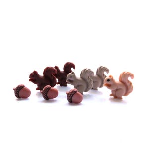 Puede incluir: Una colección de pequeños botones de plástico moldeado con forma de ardillas y bellotas. Las ardillas son de tonos marrón oscuro, marrón claro y beige, mientras que las bellotas tienen sombreros marrones texturizados y cuerpos lisos.