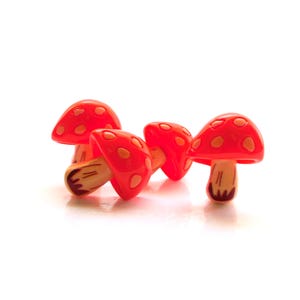May include: Four red mushroom-shaped decorative objects with white spots. The mushroom caps are a vibrant red, and the stems are a light brown color. These whimsical objects are likely used for decoration or crafting.
