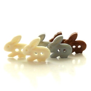 Puede incluir: Cuatro botones de plástico en forma de conejo en blanco, azul claro, marrón y beige. Los botones tienen forma de conejos con dos agujeros para coser.