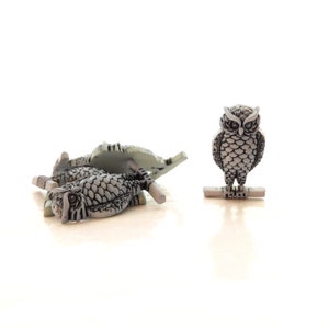 May include: Three grey owl-shaped buttons with black detailing. The owls are perched on a branch and have their wings spread out. One owl is standing upright, while the other two are lying down.