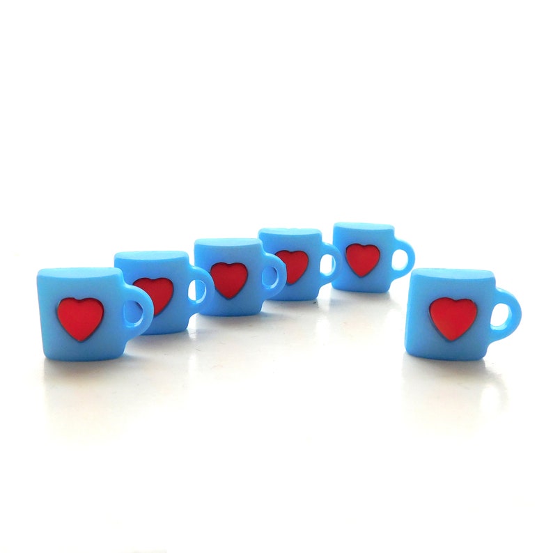 May include: Six small, light blue mugs with red heart designs. Each mug has a handle and is arranged on a white surface. The mugs are evenly spaced, with one slightly offset from the others. The overall aesthetic is simple and charming.