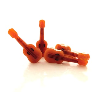 May include: Four miniature orange-brown wooden guitars, each with a different design, are arranged on a white surface.