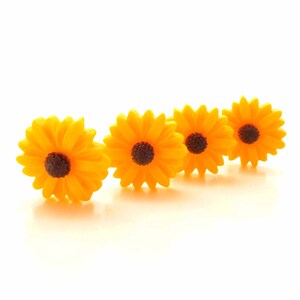 May include: Four yellow artificial sunflowers with brown centers arranged in a row on a white background.