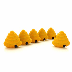 May include: Six small, yellow, cone-shaped beehive ornaments arranged in a semi-circle. Each beehive features a textured, tiered exterior with a small, dark, arched opening at the base, creating a uniform appearance across all six individual pieces.