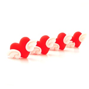 May include: Five red heart-shaped charms with white wings. The charms are arranged in a row, with the wings facing outwards.
