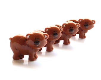 May include: A set of four small, glossy brown ceramic bear figurines arranged in a diagonal line. Each bear features a rounded body, small ears with white accents, a dark brown nose, and simple painted eyes, standing on four short legs.