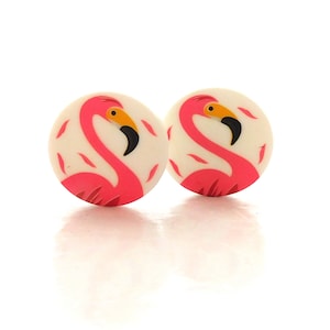 May include: Two circular buttons featuring a vibrant pink flamingo design on an off-white background. Each button displays a flamingo with a long curved neck, a yellow and black beak, and small pink feather accents scattered around the bird.