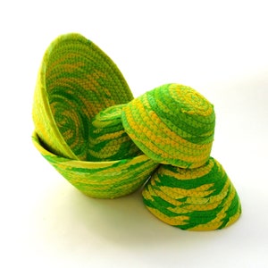 Puede incluir: Cuatro cuencos tejidos de color verde y amarillo con un patrón de espiral. Los cuencos están apilados uno encima del otro.