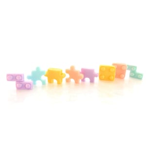 May include: A row of pastel-colored plastic puzzle pieces and blocks. The pieces are in shades of blue, yellow, orange, and purple. The blocks are a light yellow and a light pink.