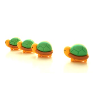 May include: Four small, green and yellow turtle figurines lined up in a row on a white background.