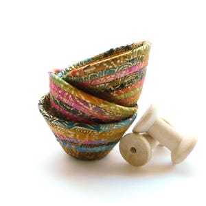 May include: A set of four colorful fabric bowls stacked on top of each other. The bowls are made from recycled fabric scraps and have a unique, handmade look.