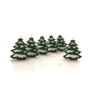 Könnte beinhalten: Sechs kleine grüne Weihnachtsbäume mit weißem Schnee oben drauf. Die Bäume sind in einer Reihe auf einer weißen Oberfläche angeordnet.