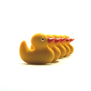May include: A line of five yellow rubber duck toys with red beaks. The ducks are lined up in a row, facing the same direction.