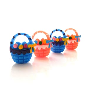 May include: Four miniature Easter baskets in a row, each with a handle and filled with colorful eggs. The baskets are blue and orange, with decorative bows and trim. A festive and cheerful Easter-themed decoration.