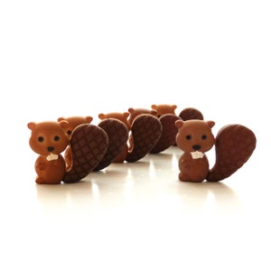 May include: A line of brown and dark brown ceramic beaver figurines. The beavers are facing the same direction, with their tails facing the viewer.